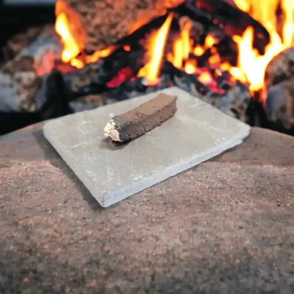 One peat incense sod with a burnt, ashy end on a grey slate, with an open fire behind