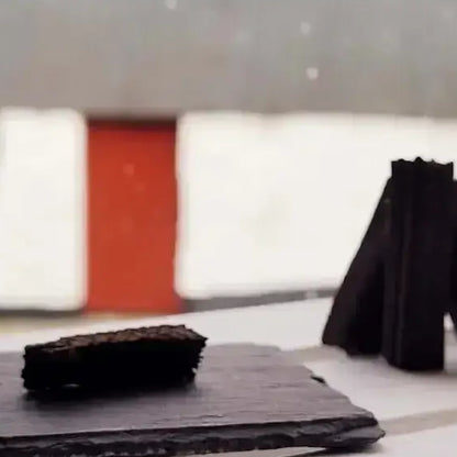 Dark turf incense sods on a black slate in front of a white wall and red door