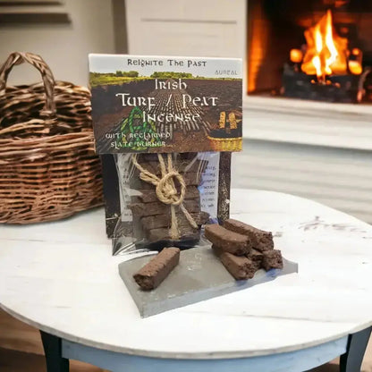 Irish Turf Peat Incense pack and turf sods on a slate, on a white table by a basket and a lit fire