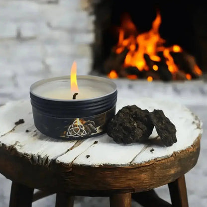 Lit black tin candle beside two pieces of turf on a wooden stool, a fire burning behind