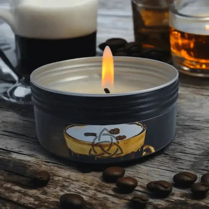Lit black tin candle with a coffee cup label on wood, coffee beans and glasses behind