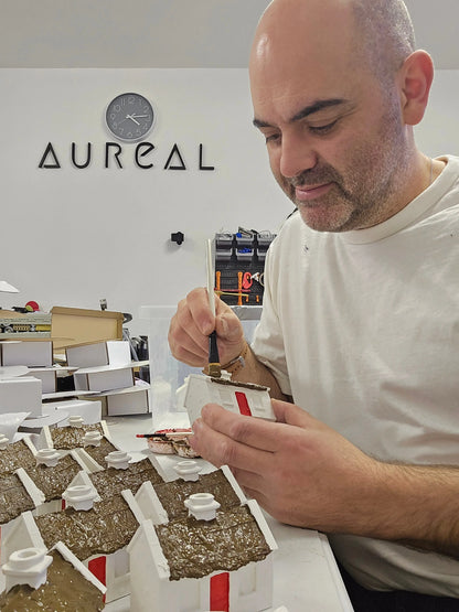 Man painting the roofs of cottage burners at a workbench below an Aureal sign